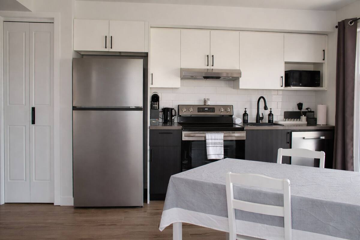 A modern kitchen with stainless steel appliances, white cabinetry, and a dining area with a table and chairs.