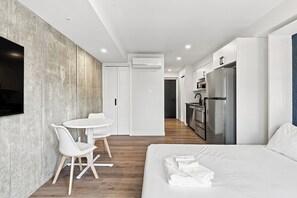 Una habitación de hotel moderna con cama, un área de comedor con sillas, una cocina con refrigerador y un equipo de aire acondicionado.