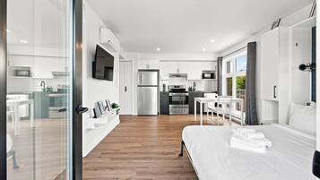 A modern hotel room with a large bed, a dining area, a kitchen, and a living area.