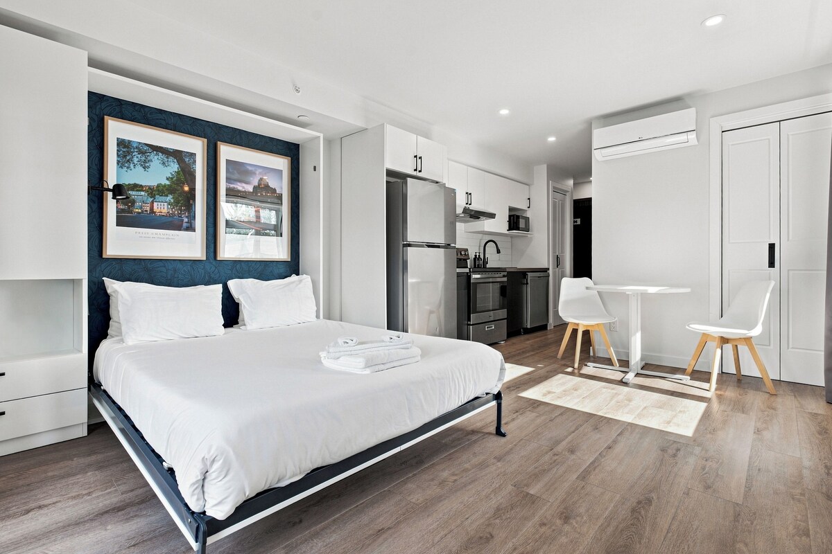 A modern hotel room with a bed, a desk, and a kitchenette.