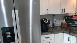 Un refrigerador Whirlpool de acero inoxidable en una cocina con armarios blancos, una cafetera y un letrero de bienvenida.