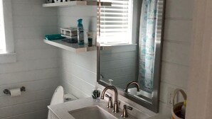 Un baño con inodoro, lavabo y espejo. Hay repisas sobre el lavabo con artículos de tocador.