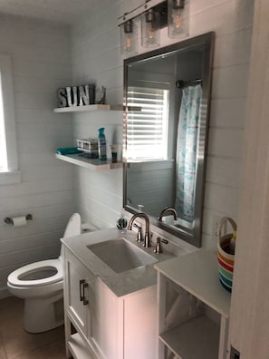 A bathroom with a toilet, sink, and mirror. There are shelves above the sink with toiletries.