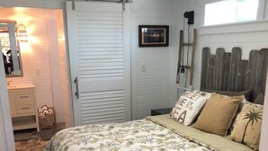Un dormitorio con una cama, ventilador de techo, ventana y puerta.