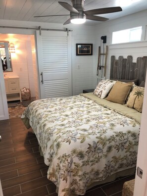 A bedroom with a bed, a ceiling fan, a window, and a door.