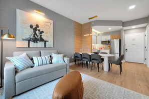 A modern living room with a grey sofa, striped pillows, a brown ottoman, and a dining area with grey chairs and a white table. - Magical Mickey Retreat, Free Shuttle, Free Parking (Orlando)
