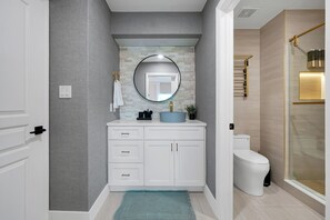 A bathroom with a white vanity, a round mirror, a toilet, and a shower area. - Magical Mickey Retreat, Free Shuttle, Free Parking (Orlando)