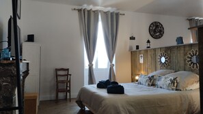 A bedroom with a bed, a chair, a wooden headboard, a wall clock, and a window with curtains. - Town House in the Heart of the Brenne (Rosnay)