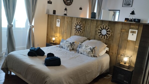 A neatly made bed with a white duvet and patterned pillows, a wooden headboard with wall-mounted decor, and a bedside table with a lamp. - Town House in the Heart of the Brenne (Rosnay)