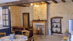Ein rustikales Interieur mit freiliegenden Backsteinwänden, einem Holztisch mit gemustertem Tischläufer, einem Kamin mit Kaminfeuer und einem Regal mit Büchern und Dekoration.