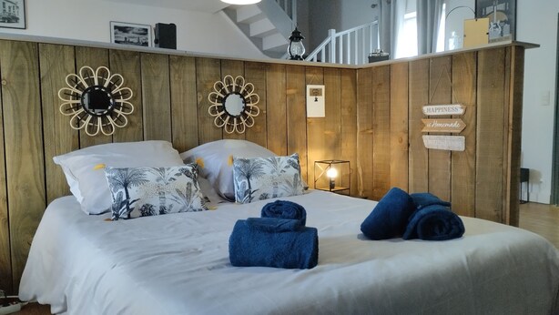 Ein Schlafzimmer mit einem hölzernen Kopfende, zwei Wanduhren und einem Bett mit weißer Bettwäsche, sowie einem Schild mit der Aufschrift 'HAPPINESS is Homemade'.