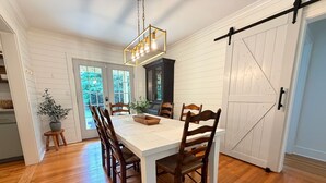 A dining area with a white table, wooden chairs, a chandelier, and a sliding barn-style door.