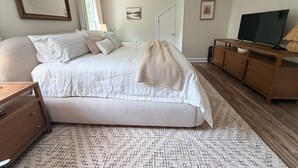 A bedroom with a large bed, a wooden dresser, a television, and a mirror.