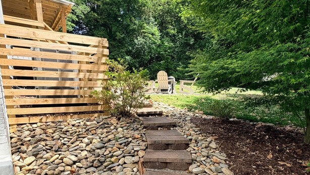 A garden pathway with stepping stones, a wooden fence, and a seating area with Adirondack chairs.