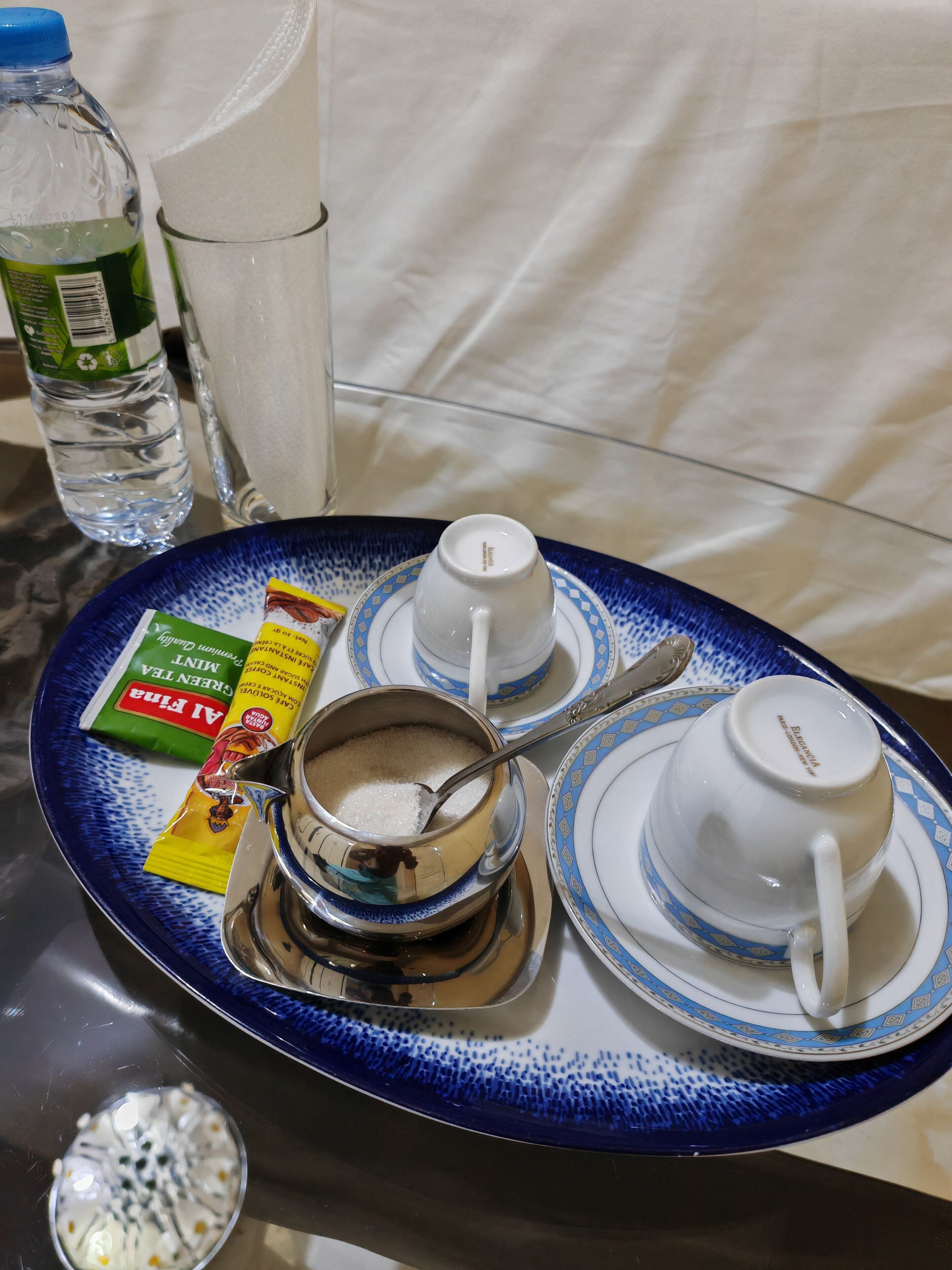 A tray with a teapot, two cups, a bottle of water, and a packet of green tea.