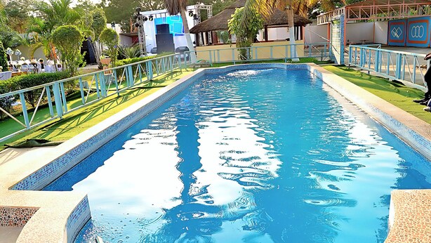 Una piscina con borde de azulejos, rodeada por una valla baja y follaje.