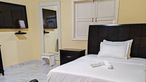 Habitación de hotel con una cama, una mesita de noche, un televisor, un espejo y una estatua.