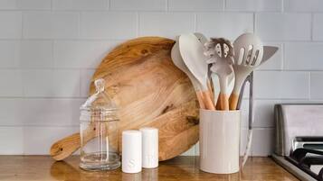 A kitchen counter with a wooden cutting board, a glass jar, salt shakers, and a utensil holder.