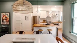 A modern kitchen with a central island, pendant lighting, and a dining area with a white table and bar stools.