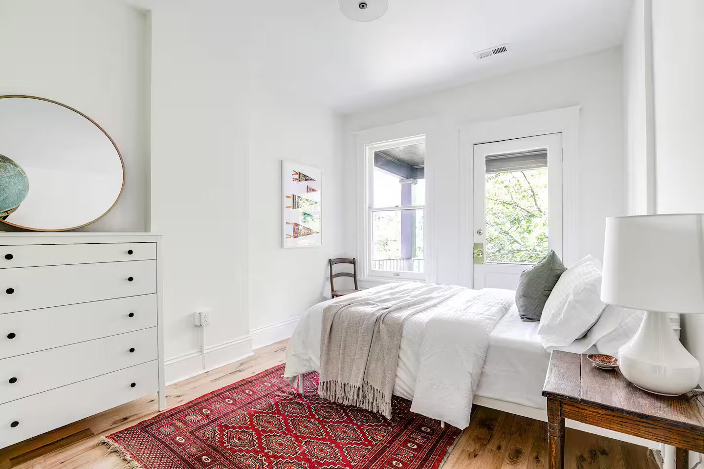 A bedroom with a bed, a dresser, a rug, a chair, and a window.