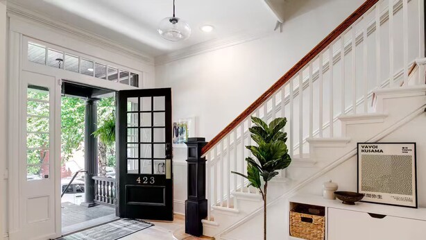 A spacious hallway with a black door marked '423,' a staircase with white railings, and a framed artwork on the wall.