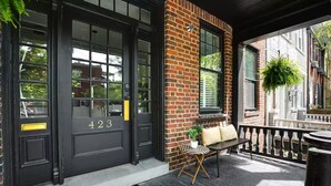 A black door with the number 423, a bench with cushions, and a 'hello' mat on the porch.