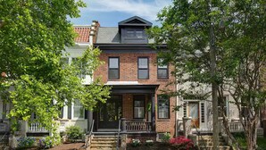 A two-story brick house with a front porch, stone steps, and a small garden.