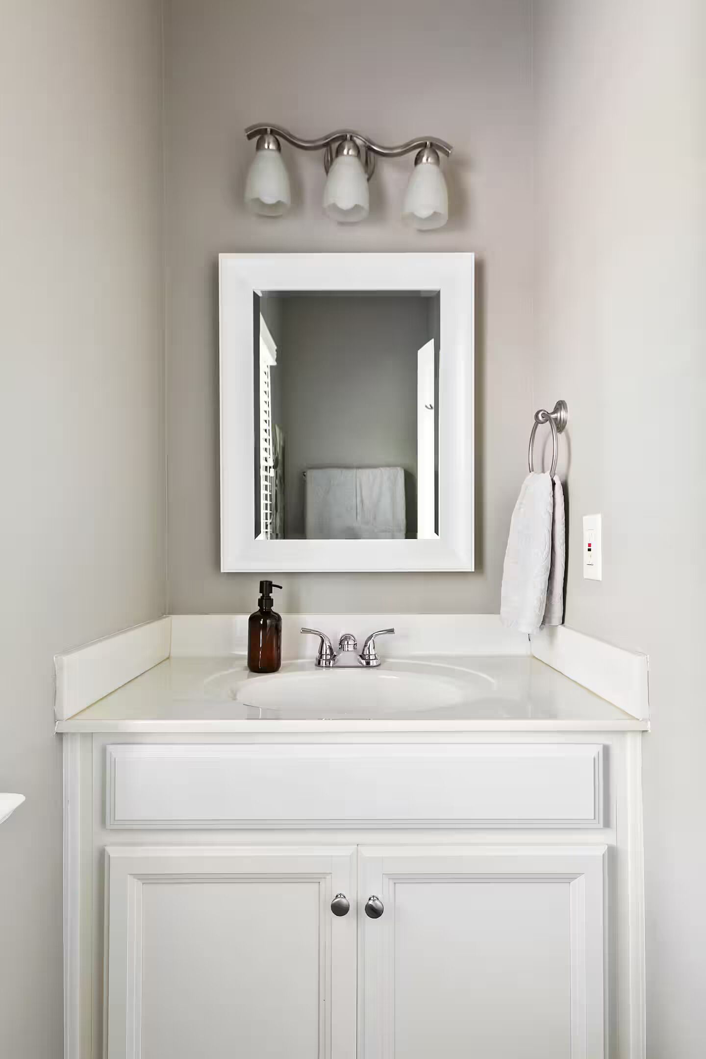 A bathroom with a white vanity, a mirror, a towel rack, and a soap dispenser.