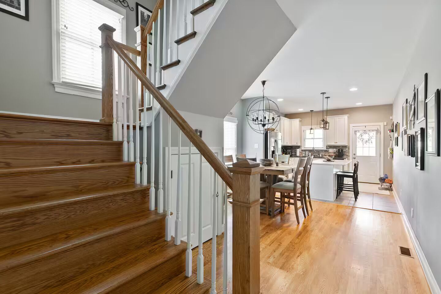 A staircase with wooden steps and white railings leading to a kitchen area with a dining table and chairs.