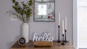 Et træbord med et spejl, en vase med grønne planter, stearinlys, et skilt og fletkurve.