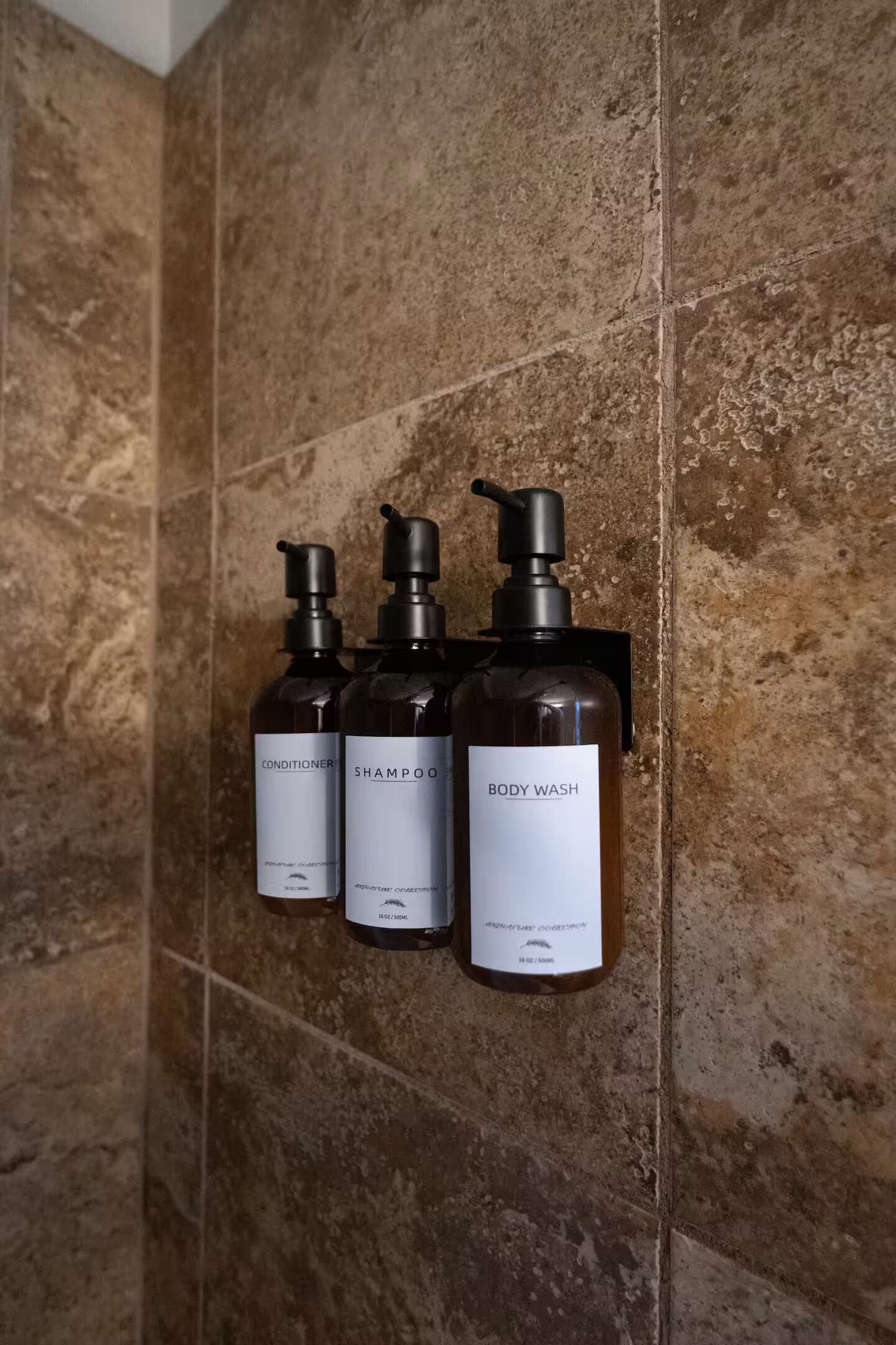 Three bottles of body wash and conditioner on a tiled wall.