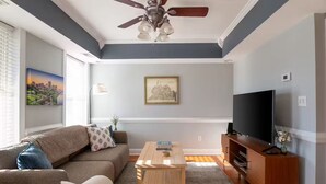A living room with a ceiling fan, a flat-screen TV, a sofa, a coffee table, and a framed picture on the wall. - Stylish Scott’s Addition Stay w/ Fire Pit & Yard (Richmond)