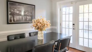 A dining room with a black table, white walls, a framed cityscape, and a vase of flowers. - Stylish Scott’s Addition Stay w/ Fire Pit & Yard (Richmond)