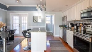 A modern kitchen with white cabinets, a stainless steel oven, and a dining area with a white island and black chairs. - Stylish Scott’s Addition Stay w/ Fire Pit & Yard (Richmond)