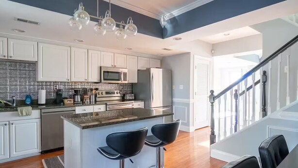 A modern kitchen with white cabinets, stainless steel appliances, and a bar area with two stools. - Stylish Scott’s Addition Stay w/ Fire Pit & Yard (Richmond)