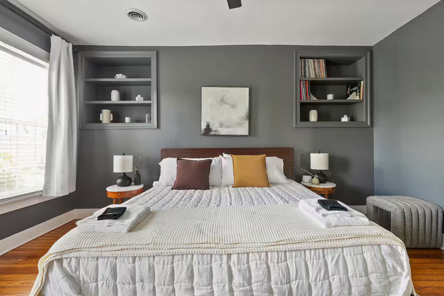 Une chambre d’hôtel moderne avec un grand lit, des tables de chevet, une bibliothèque et une fenêtre avec des rideaux.