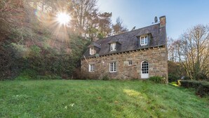 A stone house with a sloped roof, a white door, and a small garden in front. - Family home with sea view: garden & beach nearby (Ploubazlanec)