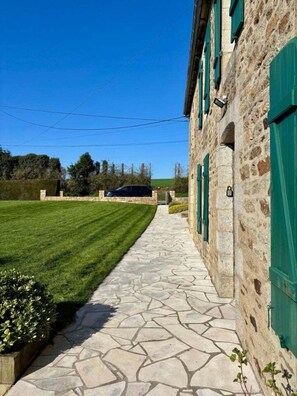 Un bâtiment en pierre avec des volets verts, un chemin en pierre et une pelouse.