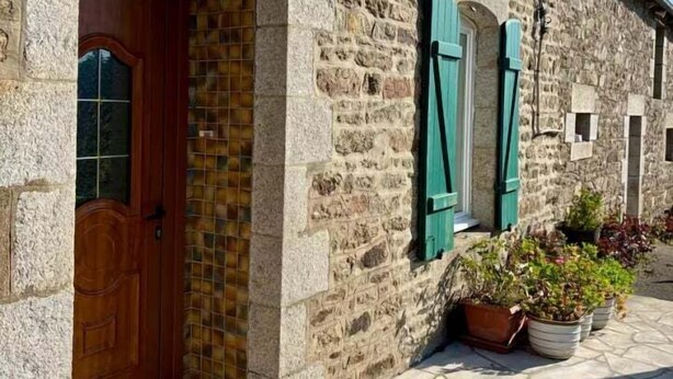 A stone building with a wooden door and green shutters, numbered 1904, with a tiled entrance and potted plants outside. - Breton longhouse with garden in Trédaniel (Trédaniel)