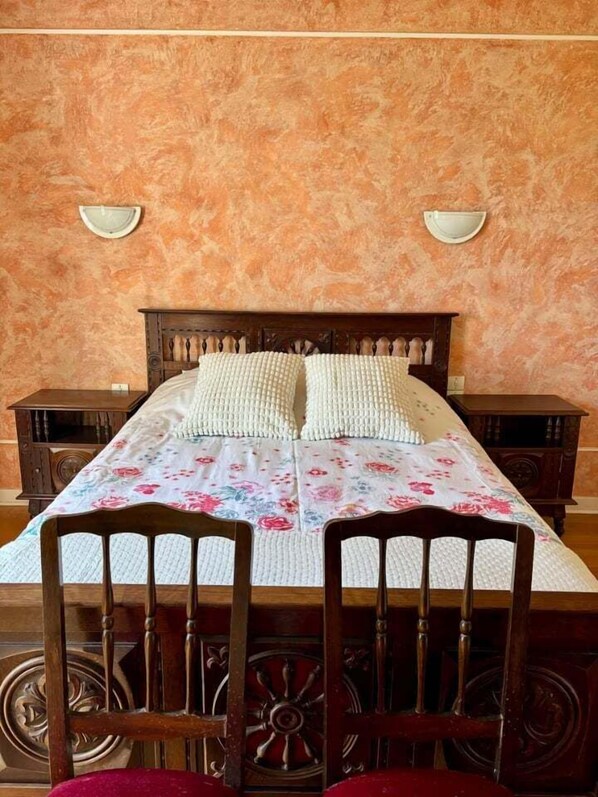 A bedroom with a wooden bed, two bedside tables, a floral bedspread, and a wall-mounted light fixture. - Breton longhouse with garden in Trédaniel (Trédaniel)