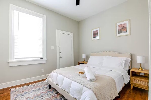 Un dormitorio con una cama, dos mesitas de noche, una ventana y dos cuadros en la pared.