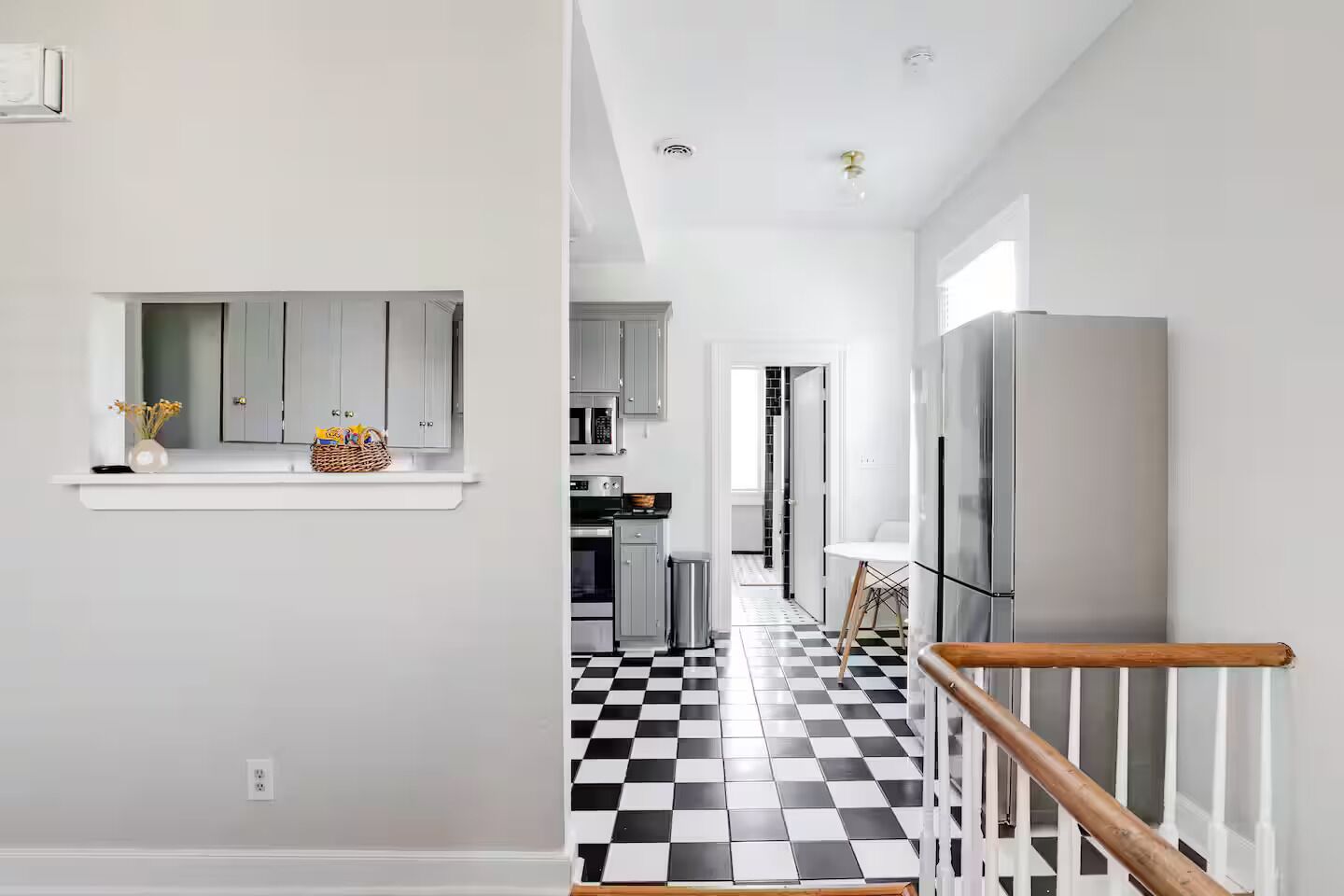 Eine moderne Küche mit grauen Schränken, einem schwarz-weißen Schachbrettboden und einem Edelstahl-Kühlschrank.