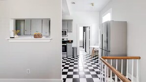 Een moderne keuken met grijze kastjes, een zwart-wit geruit vloertje en een roestvrijstalen koelkast.