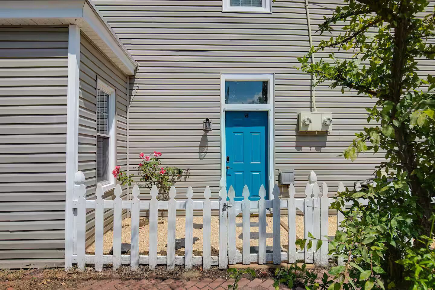 A house with a blue door, white picket fence, and a small garden with pink flowers.