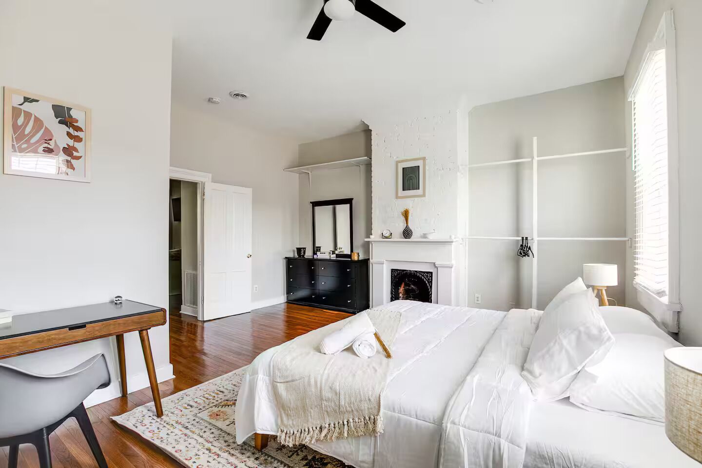 A bedroom with a bed, a desk, a chair, a fireplace, and a mirror.