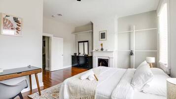 A bedroom with a bed, a desk, a chair, a fireplace, and a mirror.
