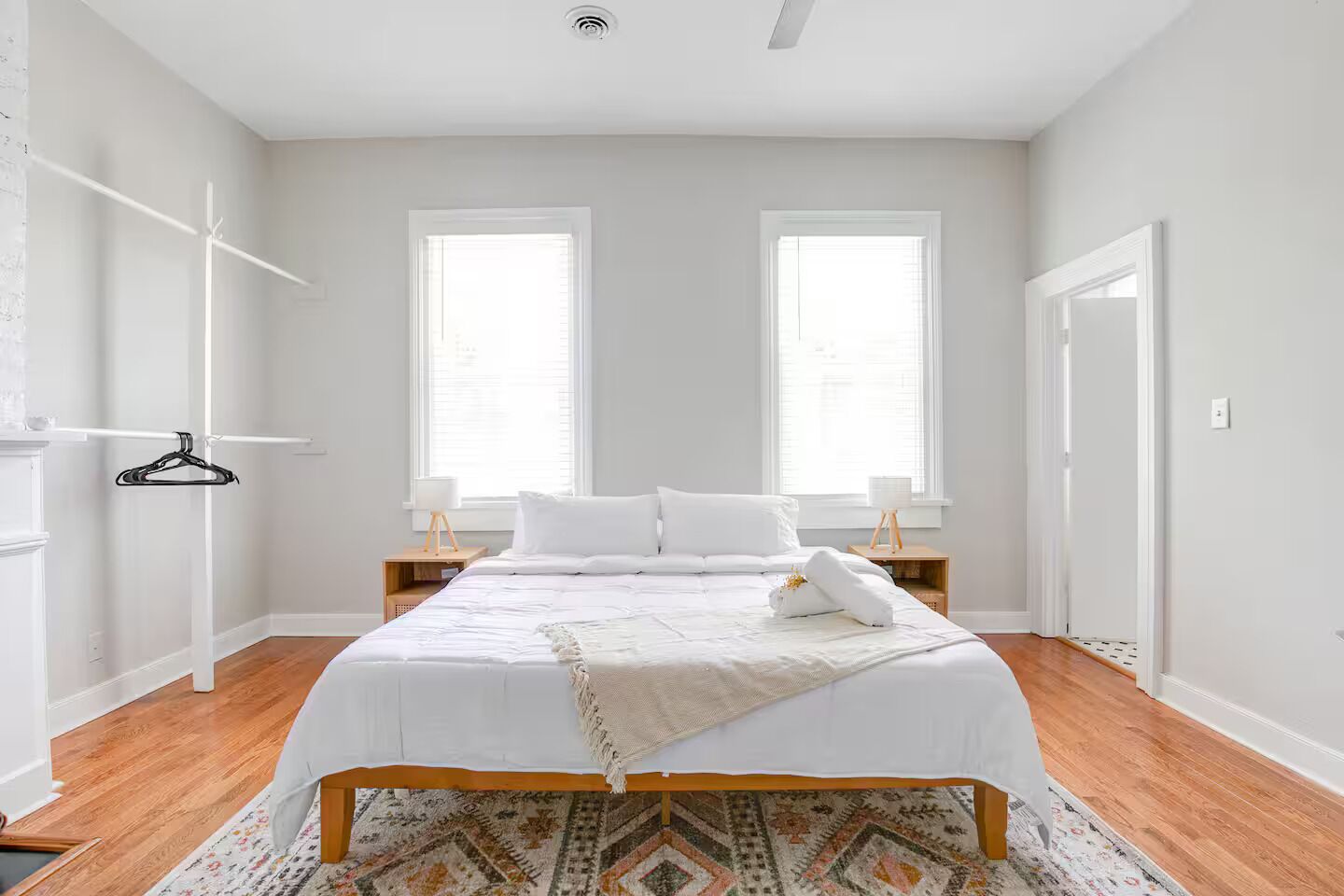 A bedroom with a bed, two windows, a wooden floor, and a hanging coat rack.