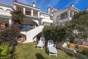 Eine Villa mit überdachter Terrasse, Sitzgelegenheiten im Freien und einer Treppe, die zum Obergeschoss führt.