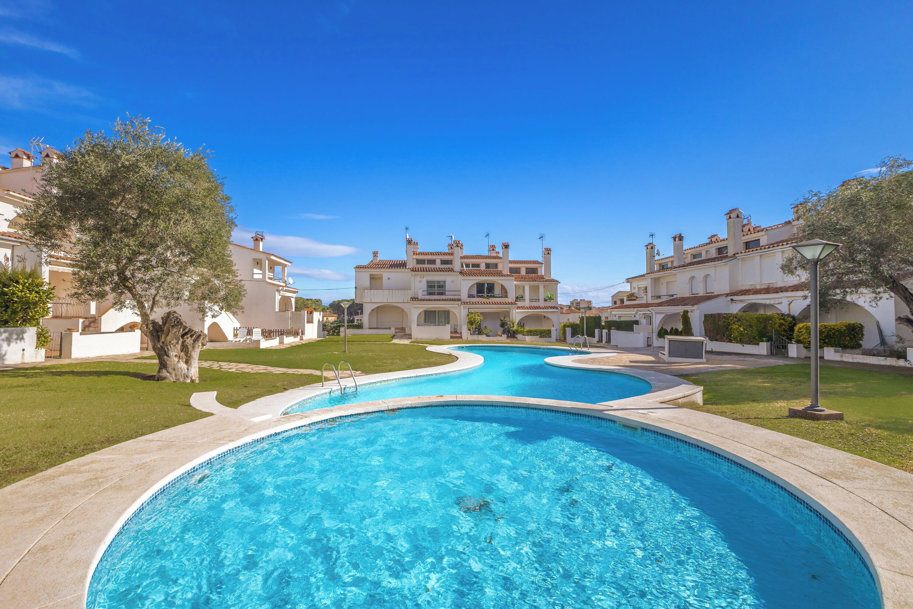 A swimming pool with a curved design, surrounded by well-maintained lawns and a large building with multiple balconies in the background.