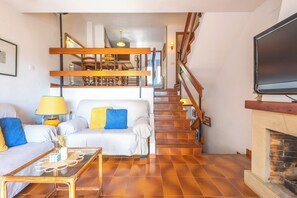Ein Wohnzimmer mit einer Couch, einem Couchtisch, einem Fernseher, einem Kamin und einer Treppe.